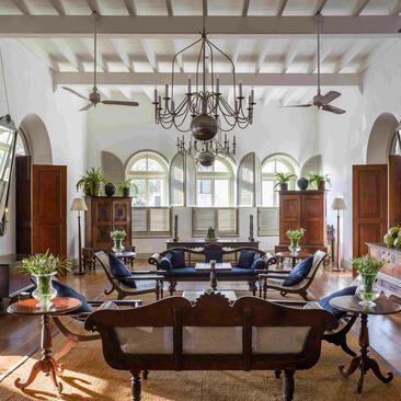Amangalla's light-filled lounge with high ceilings, ornate chandelier, and period furnishings arranged around a central seating area.