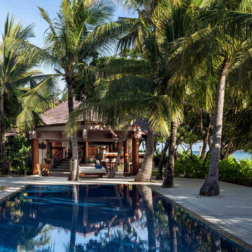 Villa con piscina de agua azul rodeada de palmeras en Amanpulo resort.