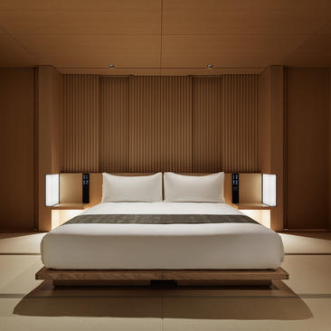 アマン京都のリゾートにある、木製パネルのヘッドボードと照明が特徴の、ミニマルな主寝室。