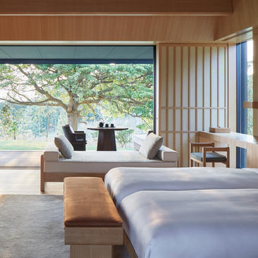 Chambre avec lit double, assise confortable et vue sur jardin boisé à Amanemu.
