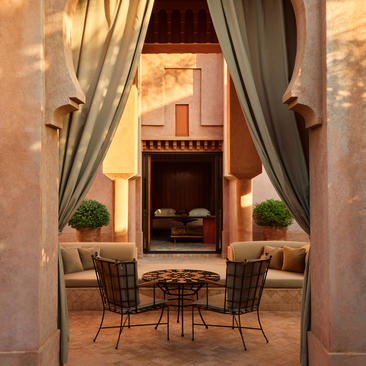 Al Hamra Suite sitting area at Amanjena, with draped curtains framing a seating space and fireplace beyond.
