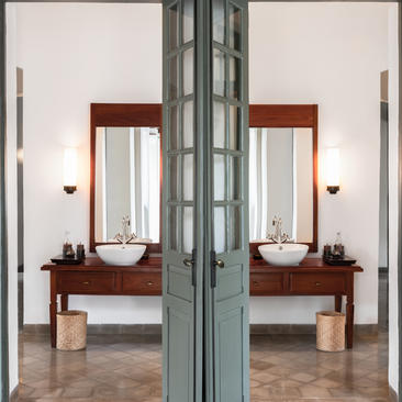 Symmetrical view of a principal bedroom at Amantaka with twin vanities, wooden furnishings and soft natural lighting.