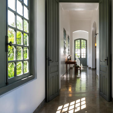 Hallway at Amantaka with dark green doors framing views towards an arched doorway, sunlight streaming across polished floors.