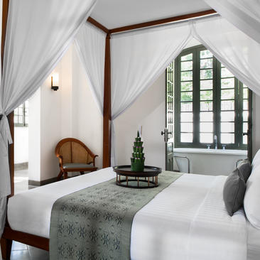 Khan Pool Suite bedroom at Amantaka with four-poster bed, arched window and calm interior.