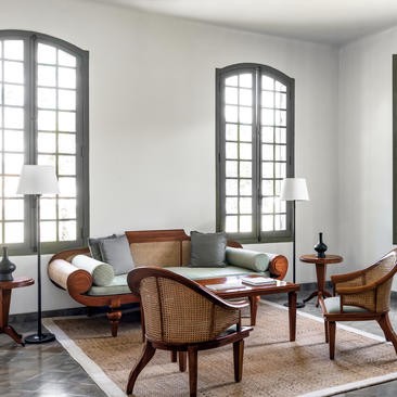 Khan Pool Suite seating area at Amantaka, with mid-century chairs, low table and tall arched windows.