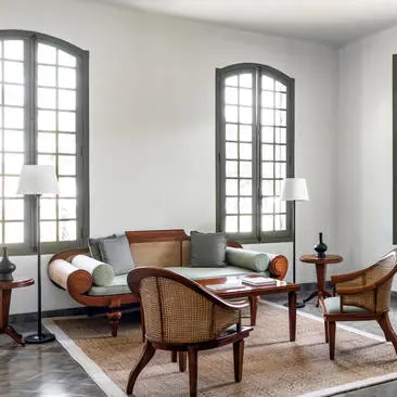 Khan Pool Suite seating area at Amantaka, with mid-century chairs, low table and tall arched windows.