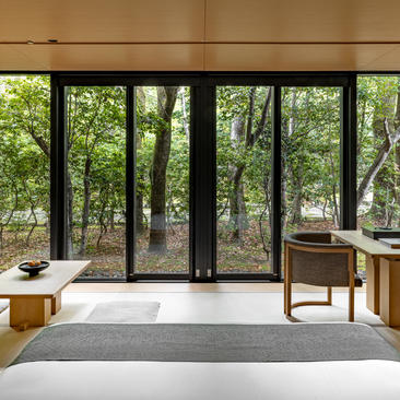 アマン京都のリゾートの寝室。大きな窓から緑の庭園を望む、落ち着いた空間。