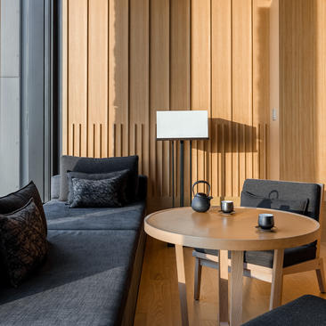 Deluxe room seating area at Aman Tokyo, with wooden slat accent wall, charcoal armchair and round timber table.