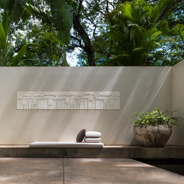 Minimalist courtyard at Amansara with white concrete wall, potted plant, and wooden bench beneath dappled tree shade.