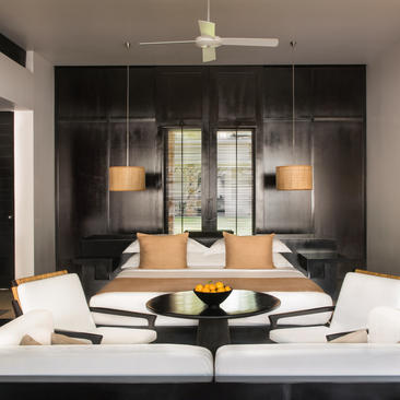 Bedroom at Amansara with black-framed glass partition, natural wood furniture, and contemporary pendant lighting.