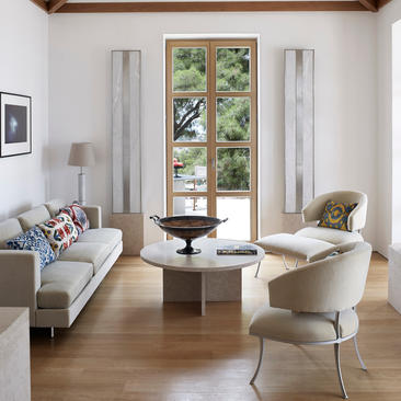 Bright living room at Amanzoe resort with cream seating, wooden flooring, and glass doors opening to garden views.