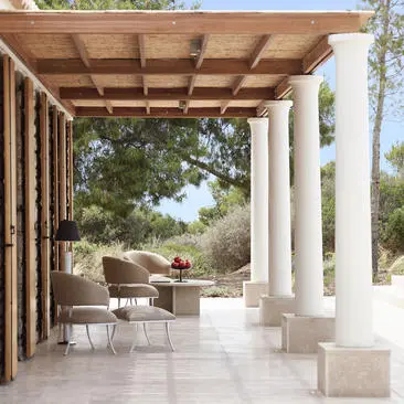Covered terrace with white columns at Amanzoe resort, overlooking gardens and seating areas.