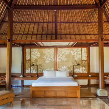 Amandari suite with wooden-beamed ceiling, platform bed and sheer curtains framing garden views.