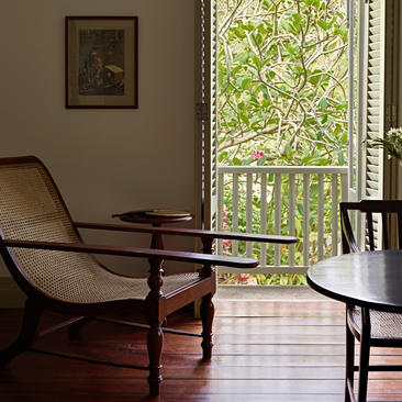 Verandah chamber at Amangalla with wooden lounge chair and side table, opening onto leafy views.