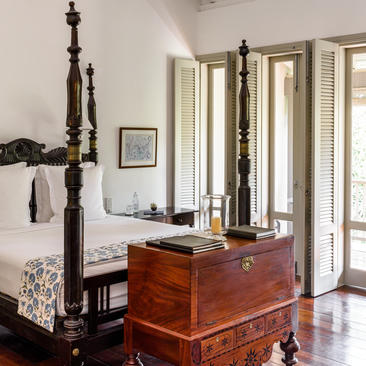 Amangalla verandah chamber with four-poster bed, wooden desk, and tall shuttered doors opening to natural light.