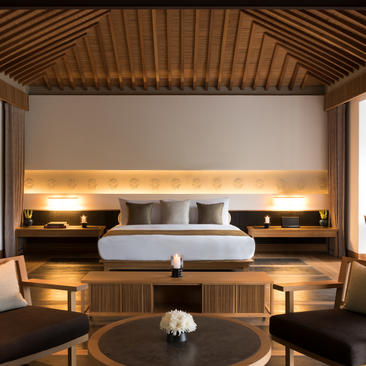 Amanoi pavilion bedroom with wooden ceiling, platform bed with integrated lighting, and seating area below.