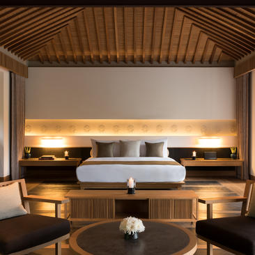 Principal bedroom at Amanoi with wooden ceiling, illuminated headboard niche, and round seating area.