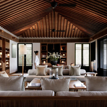 Lounge in an Amanoi residence with warm wooden ceiling, neutral furnishings, and floor-to-ceiling windows overlooking Vietnam.