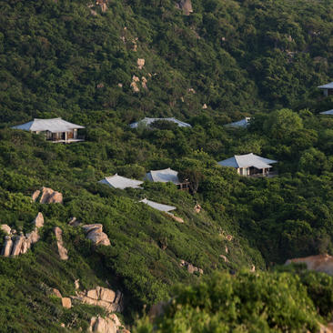 Amanoi hilltop pavilions nestled amongst forested slopes at sunrise, aerial view.