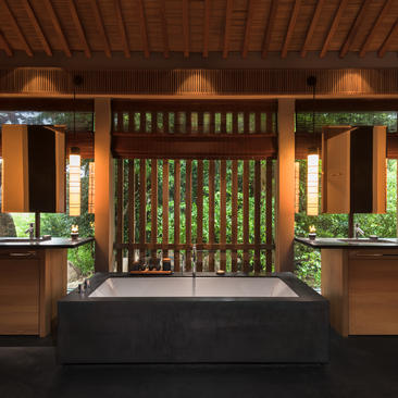 Amanoi pavilion bathroom with wooden slatted screen, sunken soaking tub, and warm ambient lighting.