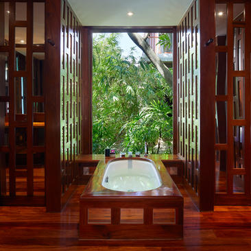 Villa bathroom with soaking tub framed by open wooden doors and garden views at Amanpuri resort.