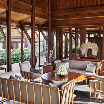 安缦璞瑞度假村木制别墅内部，宽敞起居室配有大窗户、木质家具和现代座椅。