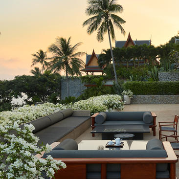 安缦璞瑞度假村的别墅外露台，配有现代低矮沙发、白色花卉和棕榈树环绕的水池景观。
