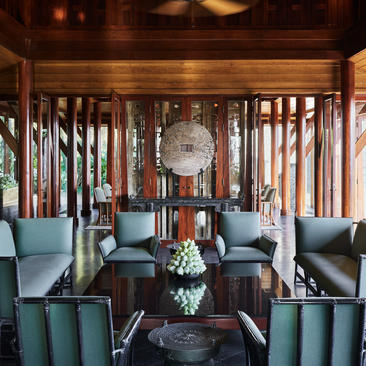 Villa lounge with teak lattice screens, dark furnishings and marble floor at Amanpuri resort.