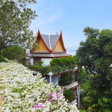 安缦璞瑞度假村的47号别墅，木质建筑屋顶与周围绿树相映，花园中绽放白色和粉色花卉。