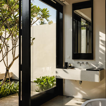 Bathroom with open door to garden courtyard at Amansara, natural light streaming across pale walls and stone sink.