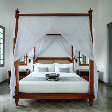 Khan Suite four-poster bed with white drapes and wooden frame at Amantaka.