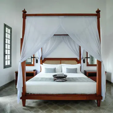 Khan Suite principal bedroom at Amantaka with four-poster bed and neutral bedding.