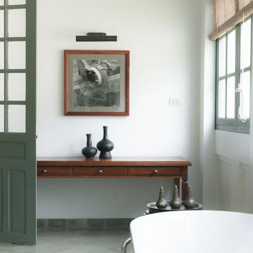 Bathroom at Amantaka with freestanding bath, wooden console table and framed artwork on pale walls.