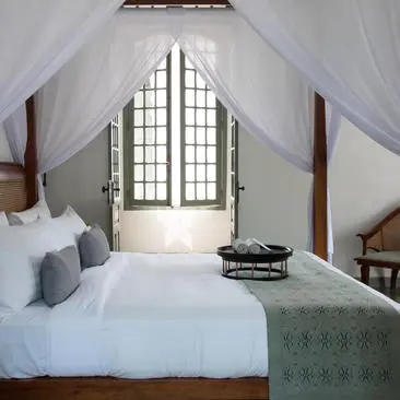 Principal bedroom at Amantaka with four-poster bed and arched window.