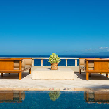 Infinity pool overlooking the Bali Sea at Amankila, with wooden loungers and clear blue sky.