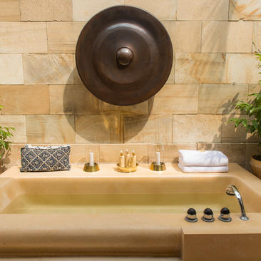 Stone bathtub with brass fixtures and circular bronze mirror at Amanjiwo.