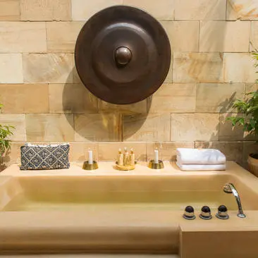 Badroom bathtub with circular bronze mirror and stone wall at Amanjiwo resort.