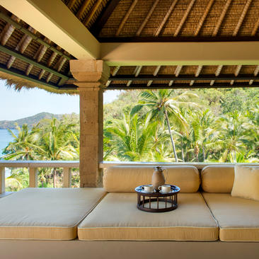 Covered pavilion at Amankila resort with cream seating, wooden beams, and views towards tropical gardens and mountains.