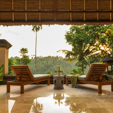 アマンダリ リゾートのシェルター付きラウンジエリア。木製の寝椅子が静かな池を囲み、緑豊かな風景を望む。