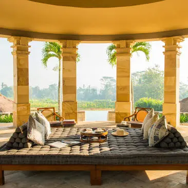 Amanjiwo resort lounge with golden columns, two seated figures, and views across terraced landscape at dawn.