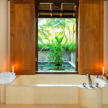 Bagno principale con vasca in travertino e vista sul giardino tropicale di Amankila.