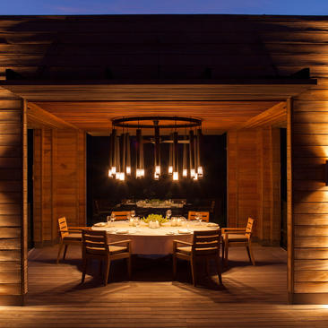 Candlelit dining pavilion at Amanoi with round table and hanging lights under wooden ceiling.