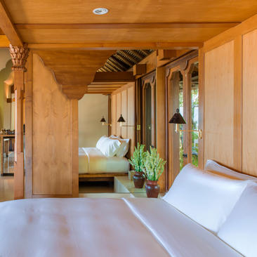 Wooden pavilion interior at Amankila resort with bed, plant and arched doorway.