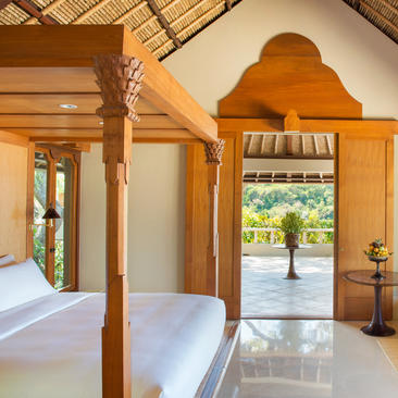 Wooden four-poster bed in a light-filled bedroom at Amankila, with open doors revealing a tropical garden view.