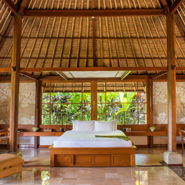 アマンダリ リゾートの木造建築の寝室。天井が高く、大きな窓から緑が見える。