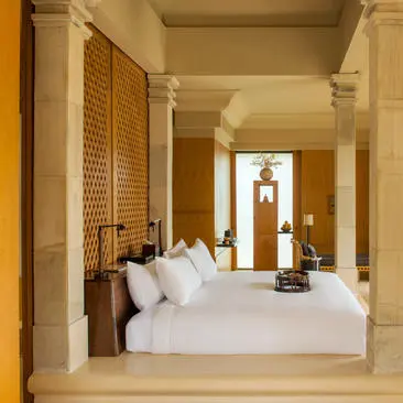 Kasur berukuran queen dengan bantal putih di kamar tidur resort Amanjiwo, kolom putih dan dinding terracotta.