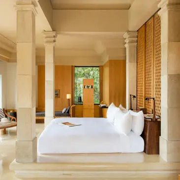 Spacious principal bedroom at Amanjiwo resort with stone columns, wooden accents, and white bedding.