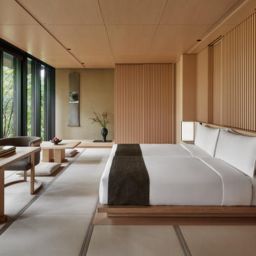アマン京都のリゾートにある、木製パネルと大きな窓を備えた落ち着いた寝室。
