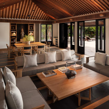 Amanoi dining pavilion with wooden table, grey seating and open doors to garden.