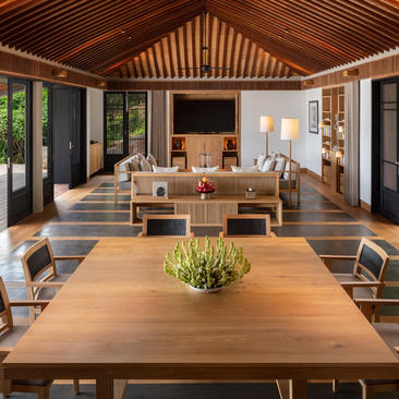 Amanoi dining pavilion with wooden table, chairs, and open doors overlooking verdant surroundings.